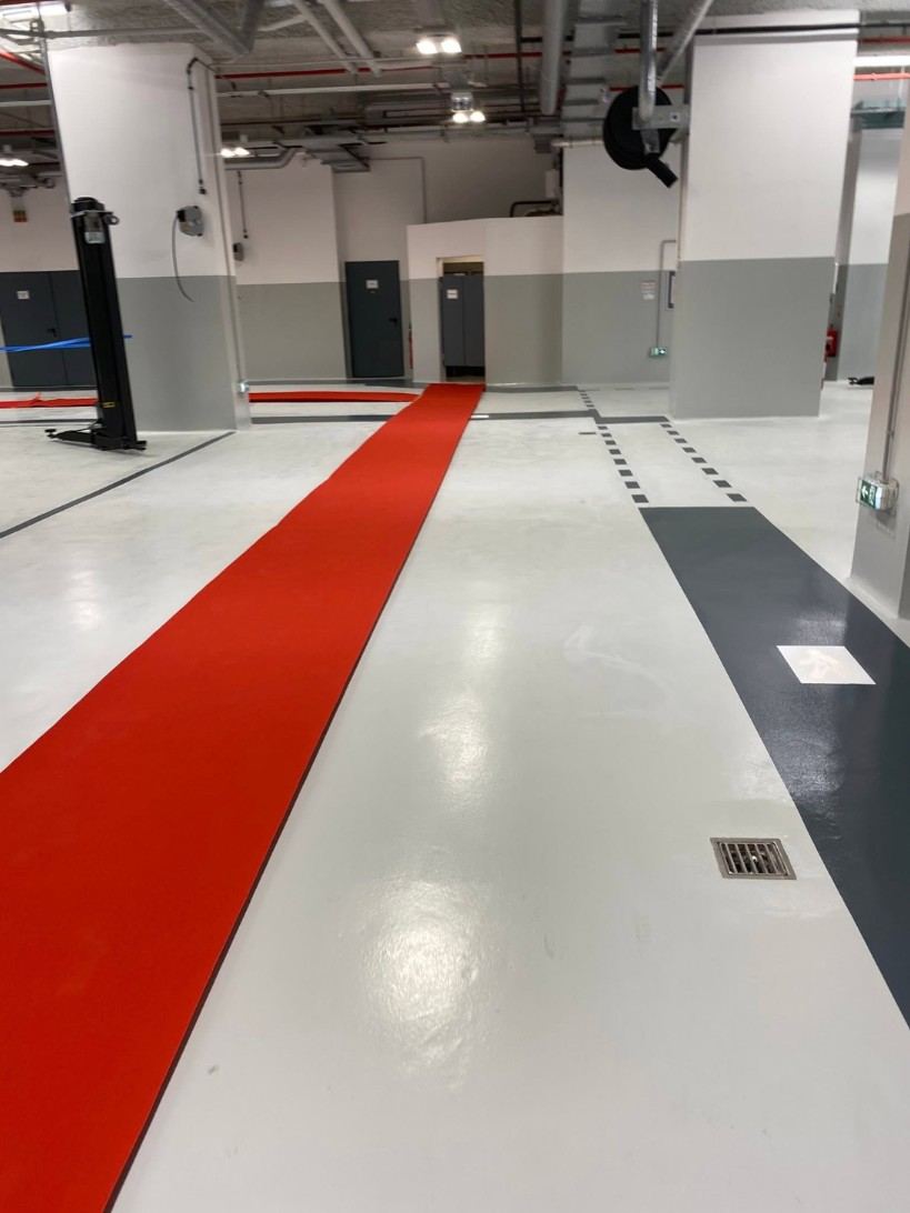 Atelier en résine claire bordée de bandes anthracite, tapis rouge déroulé